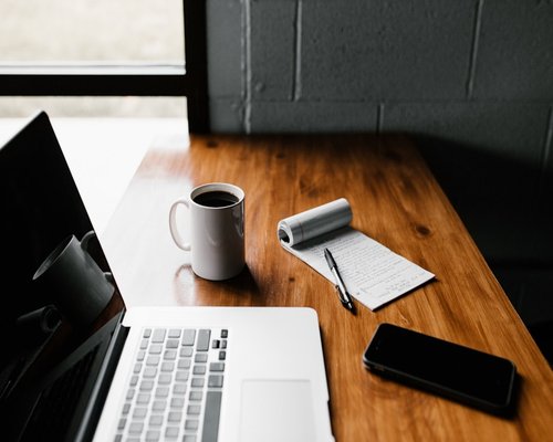 A cup of coffee next to a notebook on a wooden desk